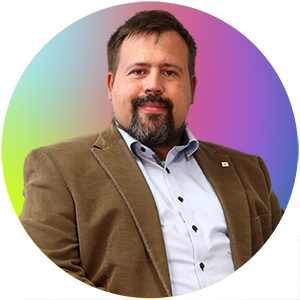 Auf dem Bild ist Herr Stefan Kamer. Er trägt einen braunen Blazer über einem hellblauen Hemd.